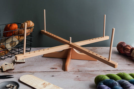 Amish yarn swift on a wooden table surounded by Woollen Wytch yarn supplies including hand dyed yarn and a sock ruler